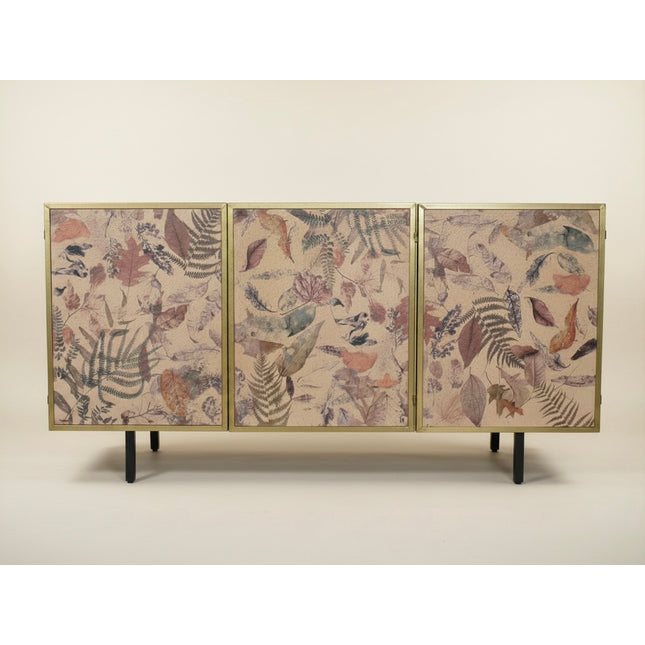 A three-panel sideboard or credenza with a gold-toned frame, featuring botanical leaf patterns in muted pink, brown, gray, and blue on a light beige background, supported by slim black legs against a plain light beige studio backdrop - Elderflower Lane