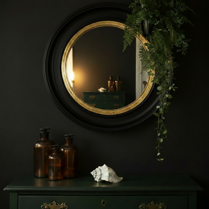 Black and gold convex mirror styled against a dark moody wall with green vintage chest of drawers and brown apothecary bottles